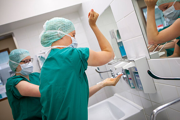 Zwei medizinische Fachkräfte bereiten sich auf eine OP vor und desinfizieren sich Hände und Arme. 