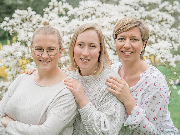 3 Mitarbeiterinnen vom TEam der Hebammenpraxis Elmshorn vor einem Magnolienstrauch.