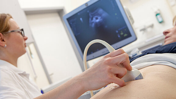 Medizinische Fachkraft hält das Sonografiegerät auf den Bauch der Patientin.