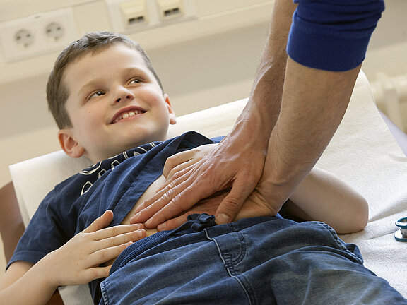 Ein Junge liegt auf einer Untersuchungsliege während ein Mediziner seinen Bauch abtastet.