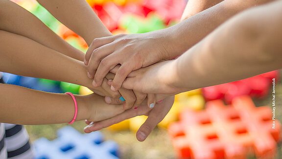 Sieben Kinderhände übereinander treffen in der Mitte zusammen.