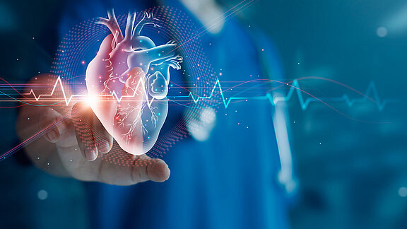 Ein Herzsymbol mit Herzschlag wird virtuell von einer medizinischen Fachkraft, die im Hintergrund steht, angetippt.