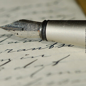 Handschriftlich beschriebenes Blatt Papier und die Spitze eines Füllfederhalters