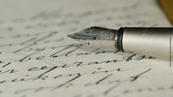 Handschriftlich beschriebenes Blatt Papier und die Spitze eines Füllfederhalters