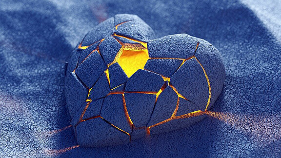 Ein brüchiges blaues Herz liegt auf blauem Untergrund und leuchtet golden von innen.