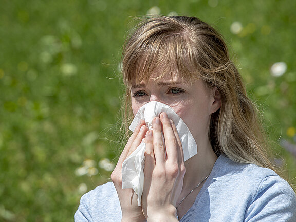 Jugendliche draußen auf einer grünen blühenden Wiese schnäuzt ins Taschentuch.
