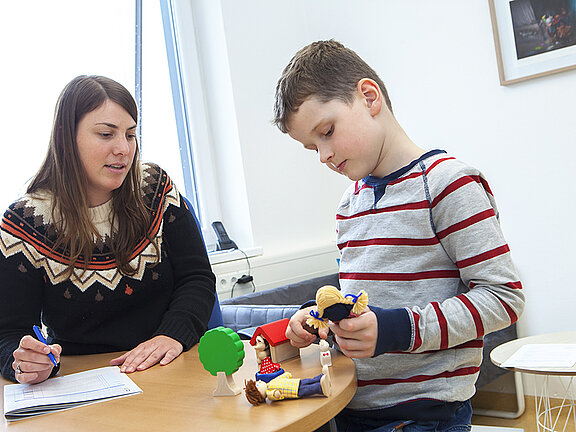 Eine Psychologin unterhält sich mit einem Jungen, der mit Spielzeugfiguren spielt.