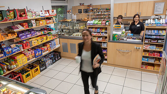 Eine Besucherin hat im Kiosk eingekauft, hinterm Tresen stehen zwei Mitarbeitende.