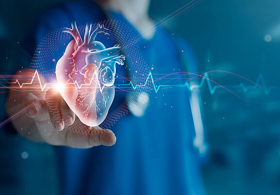 Ein Herzsymbol mit Herzschlag wird virtuell von einer medizinischen Fachkraft, die im Hintergrund steht, angetippt. 