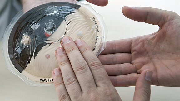 Hände tasten ein Brustmodell ab.