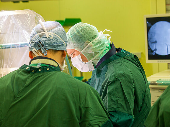Zwei Operateure in OP-Kleildung im OP-Saal sind konzentriert auf die Operation.