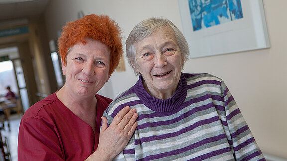 Eine Pflegefachkraft ist mit einer Patientin auf dem Flur der Geriatrischen Tagesklinik unterwegs.