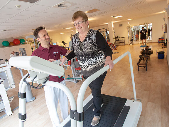 Ein Physiotherapeut leitet eine Patientin auf dem Laufband im MediFit an.