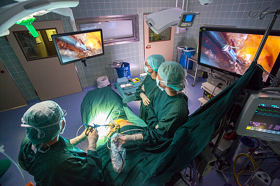 Minimalinvasive Operation im OP-Saal, drei medizinische Fachkräfte stehen am OP-Tisch und blicken auf den OP-Monitor.