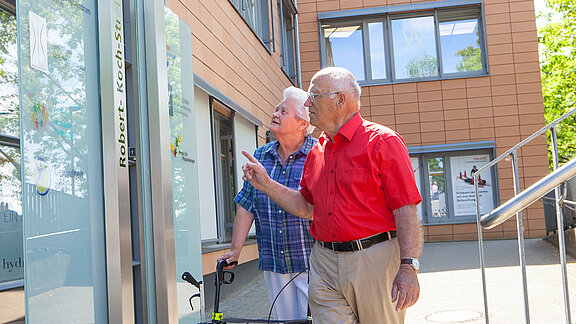 Ein Mann und eine Frau mit Rollator stehen vor dem Ärzte- und Dienstleistungszentrum.