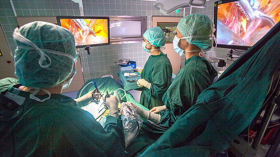 Operartionssituation eines minimal-invasiven Eingriffs, Operateur und med. Fachkräfte blicken auf den OP-Monitor.